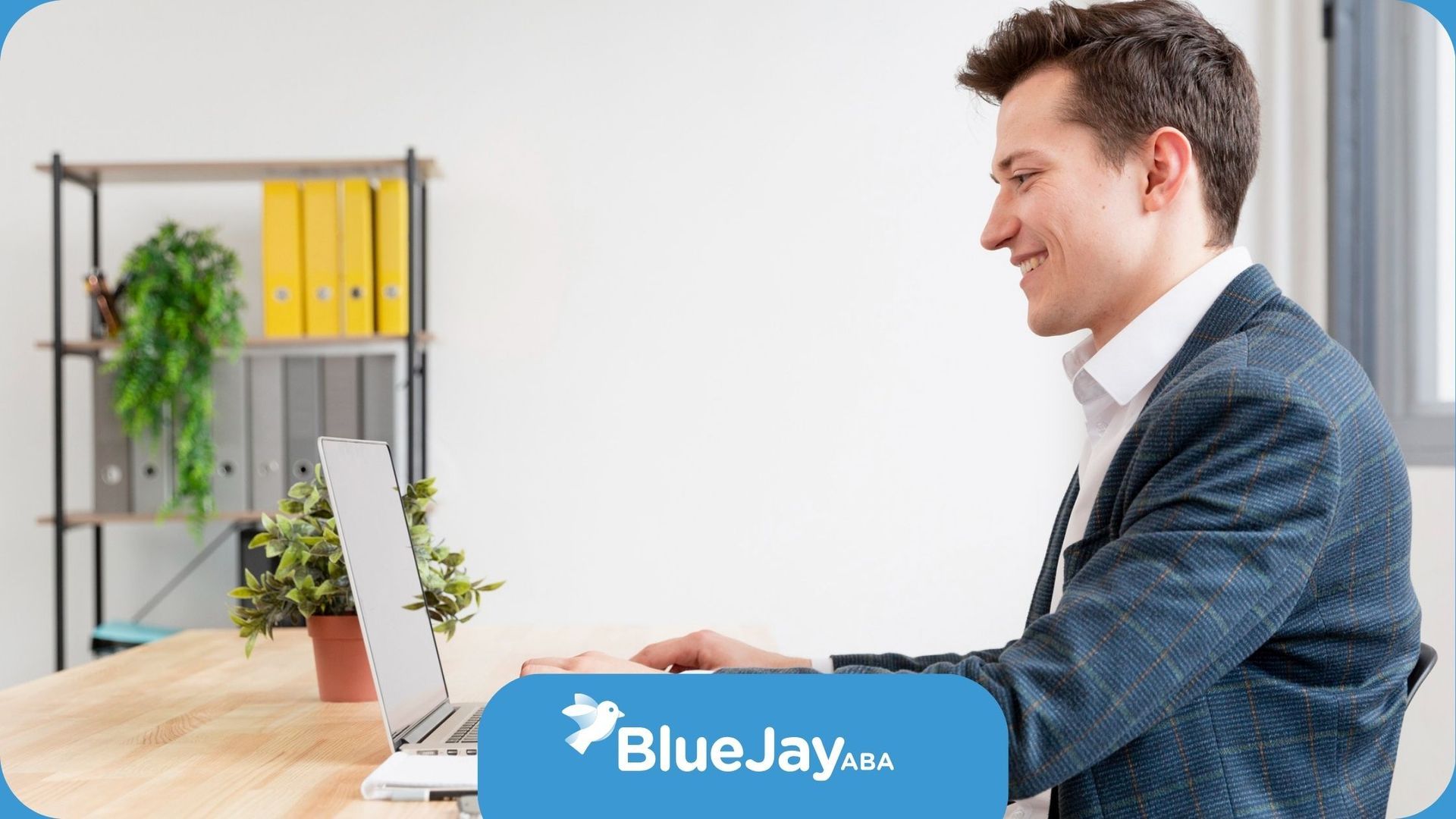 An autistic man in a suit is sitting at a desk using a laptop computer.