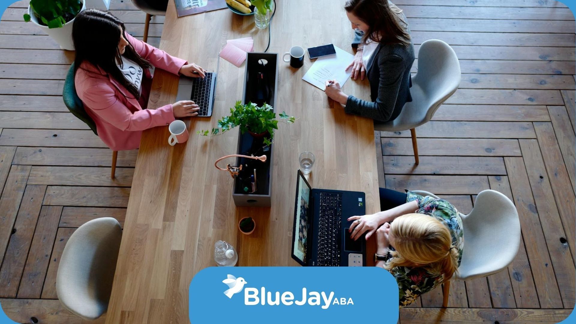 Overhead view of a wooden table with autistic professionals working on laptops in Massachusetts.