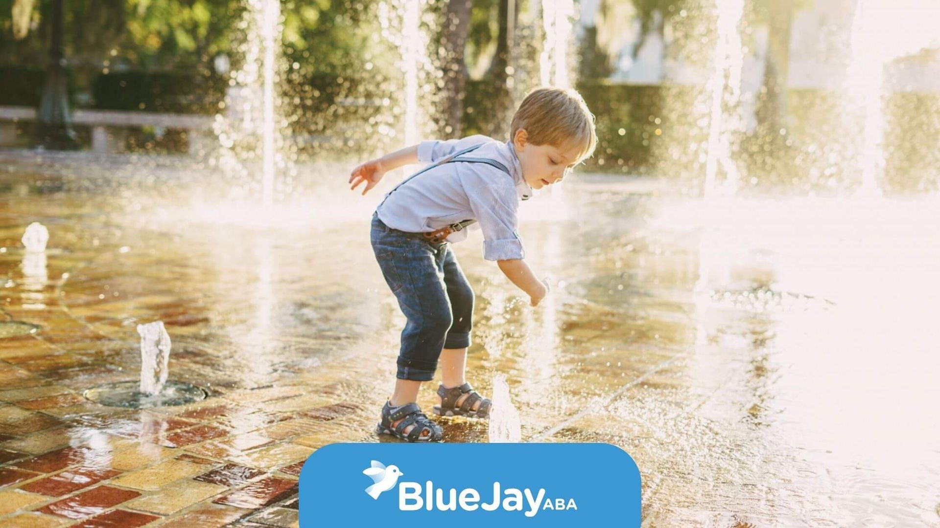 Young boy with autism playing in a splash fountain on a sunny day.