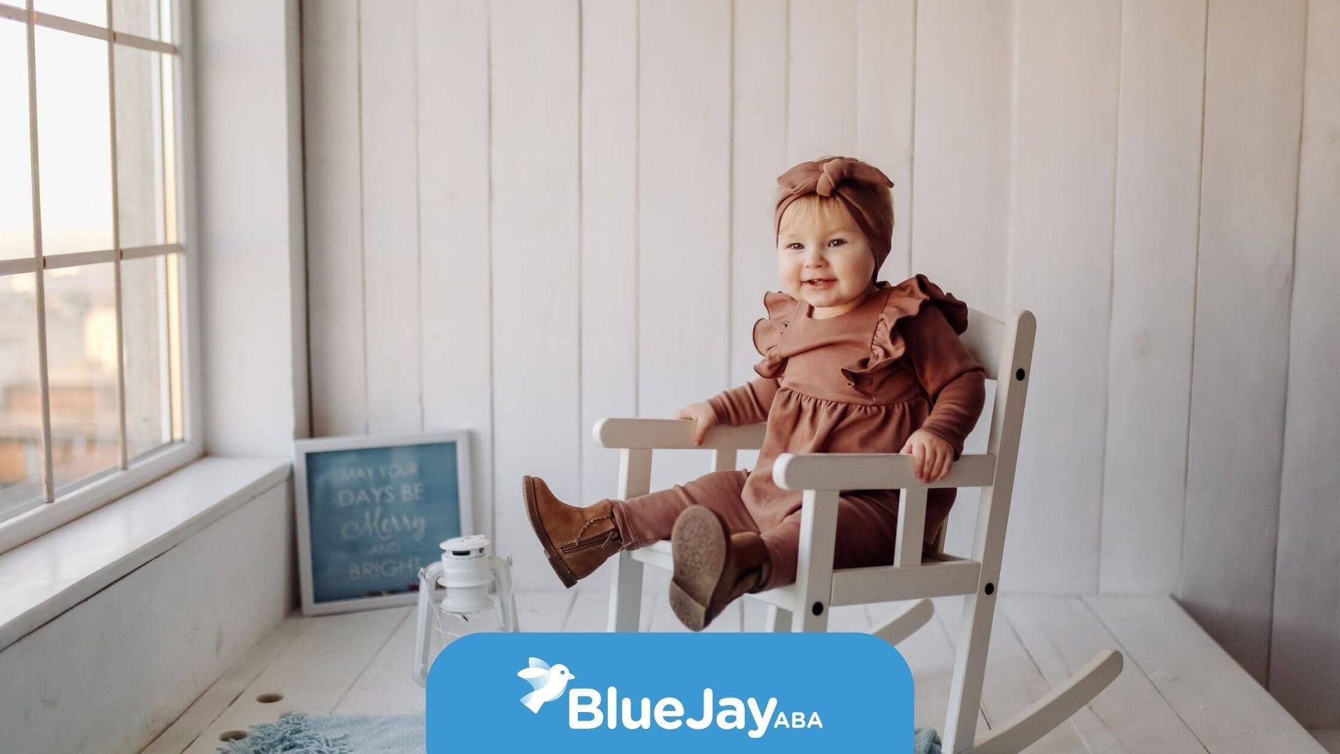 Happy autistic baby sitting in a rocking chair, smiling in a cozy, minimalistic room after therapy.