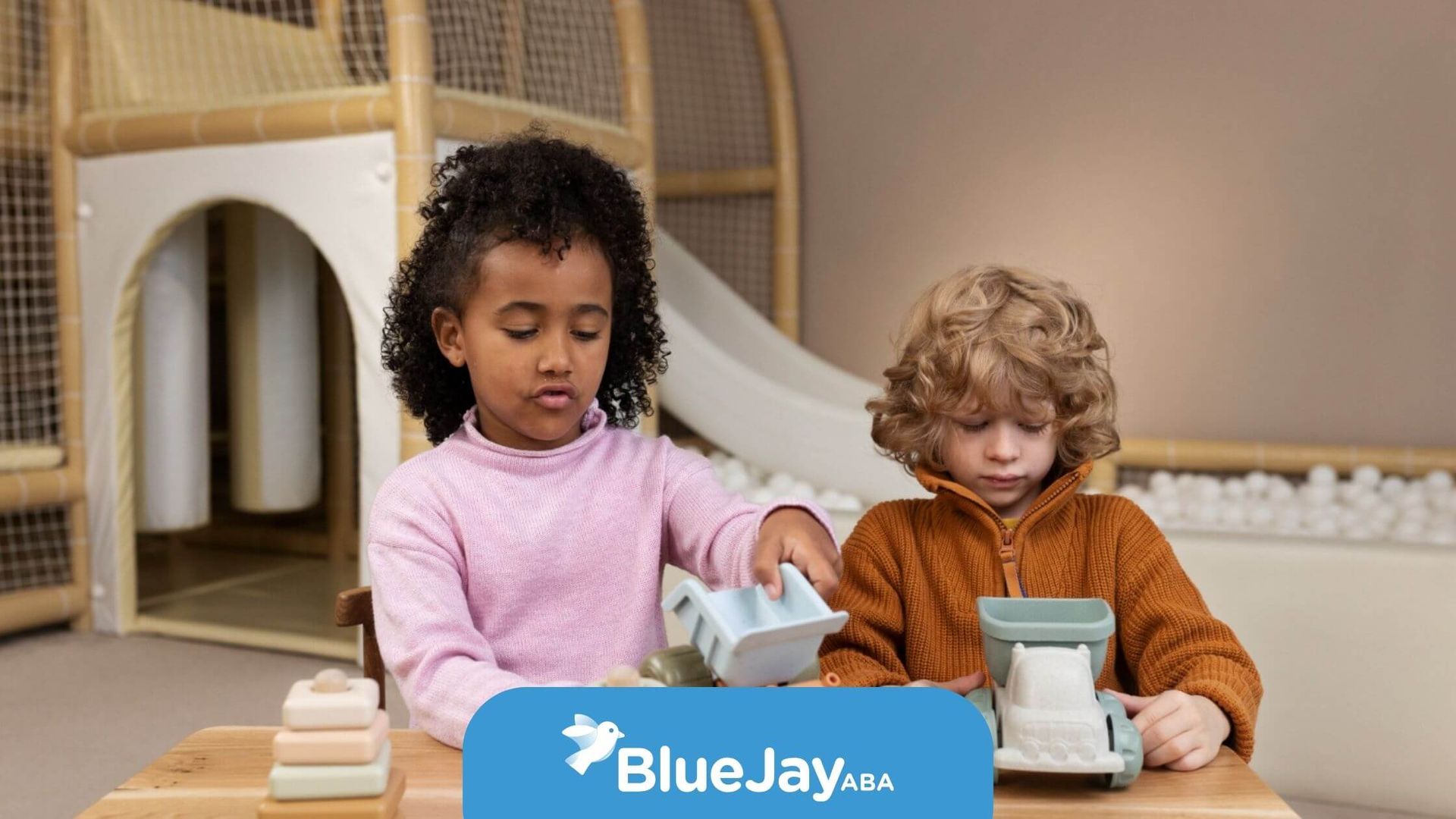 Two young children with autism sitting at a wooden table in a playroom during ABA therapy.