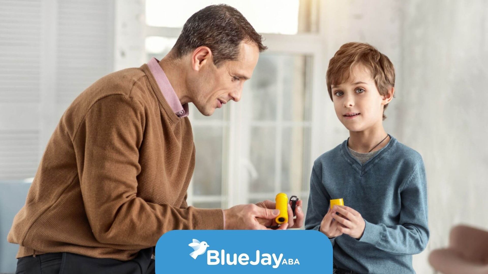A male BCBA and a young boy sit on a wooden table together in ABA therapy.