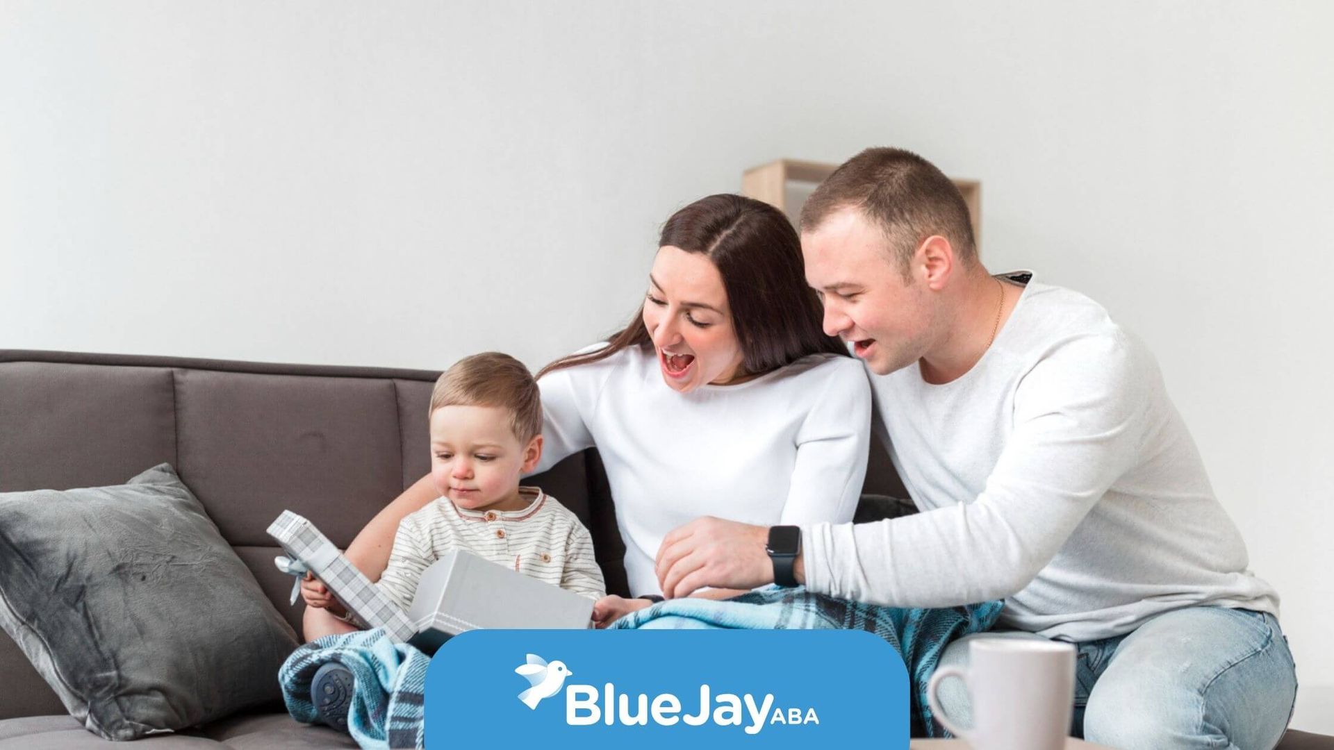 Family reading a book together on a couch; parents smiling, child looking at book.