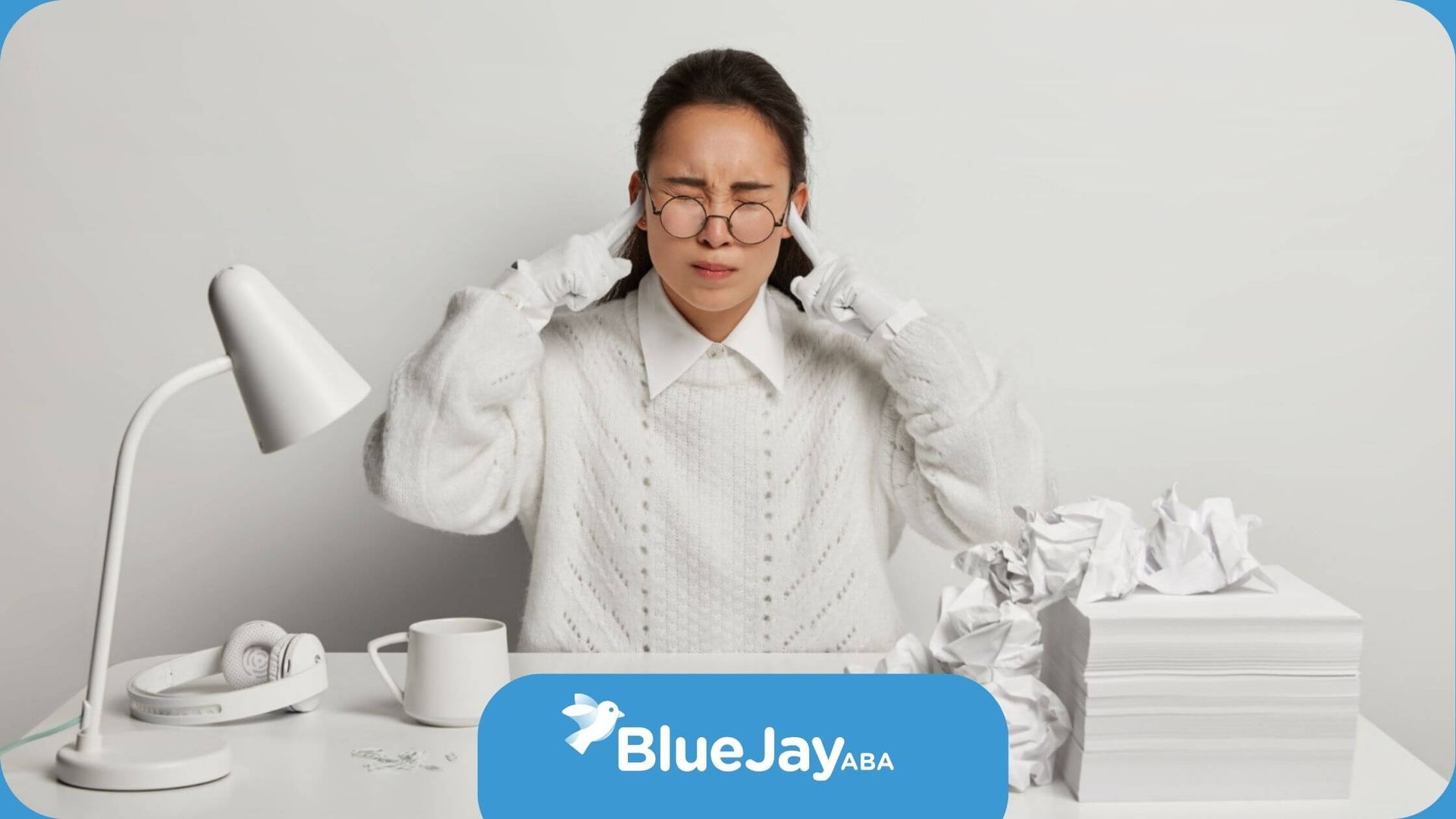 A woman with autism glasses pressing her temples with a stressed expression at a desk.