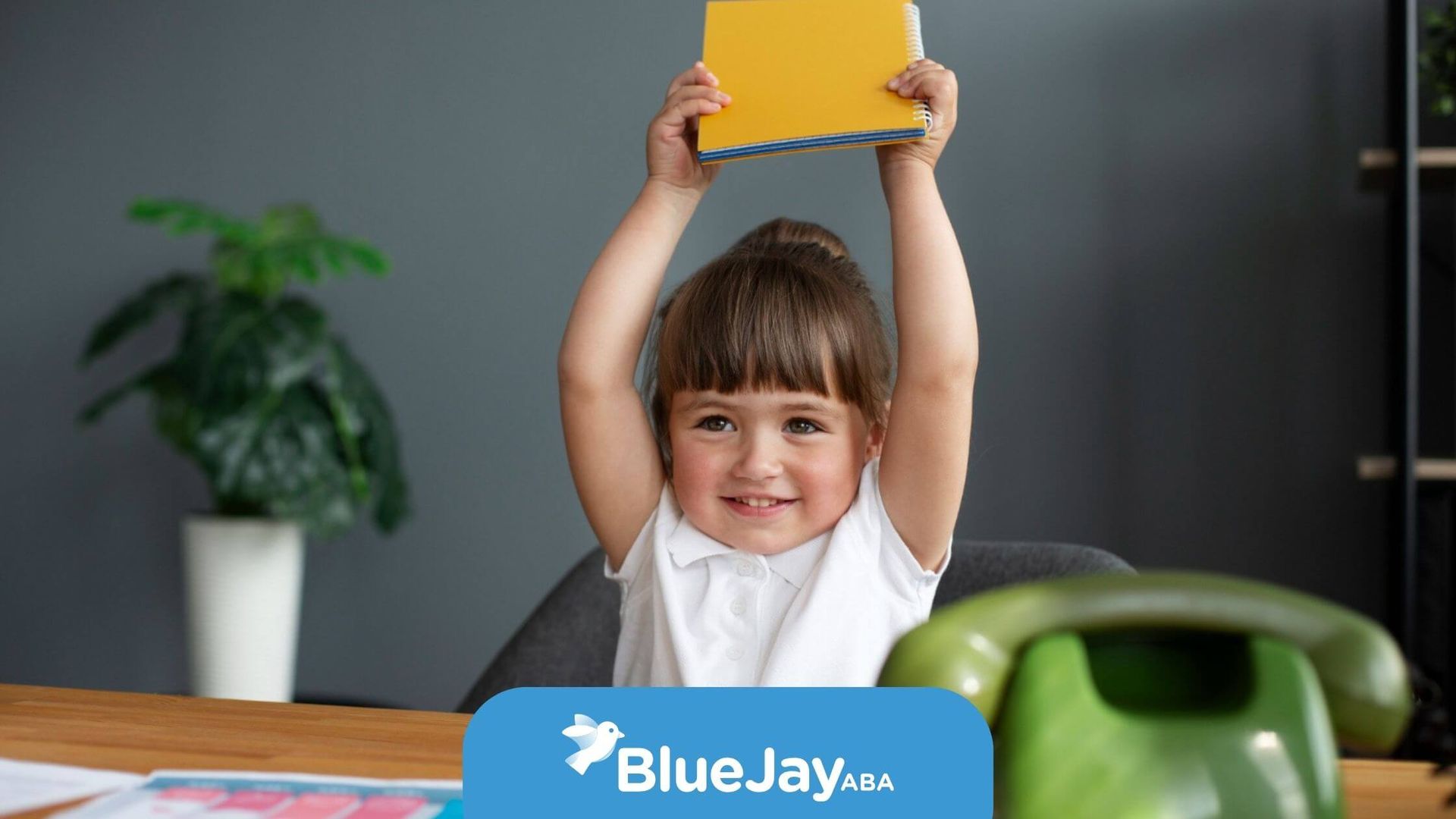 Girl with autism holding notebook over head in ABA therapy.
