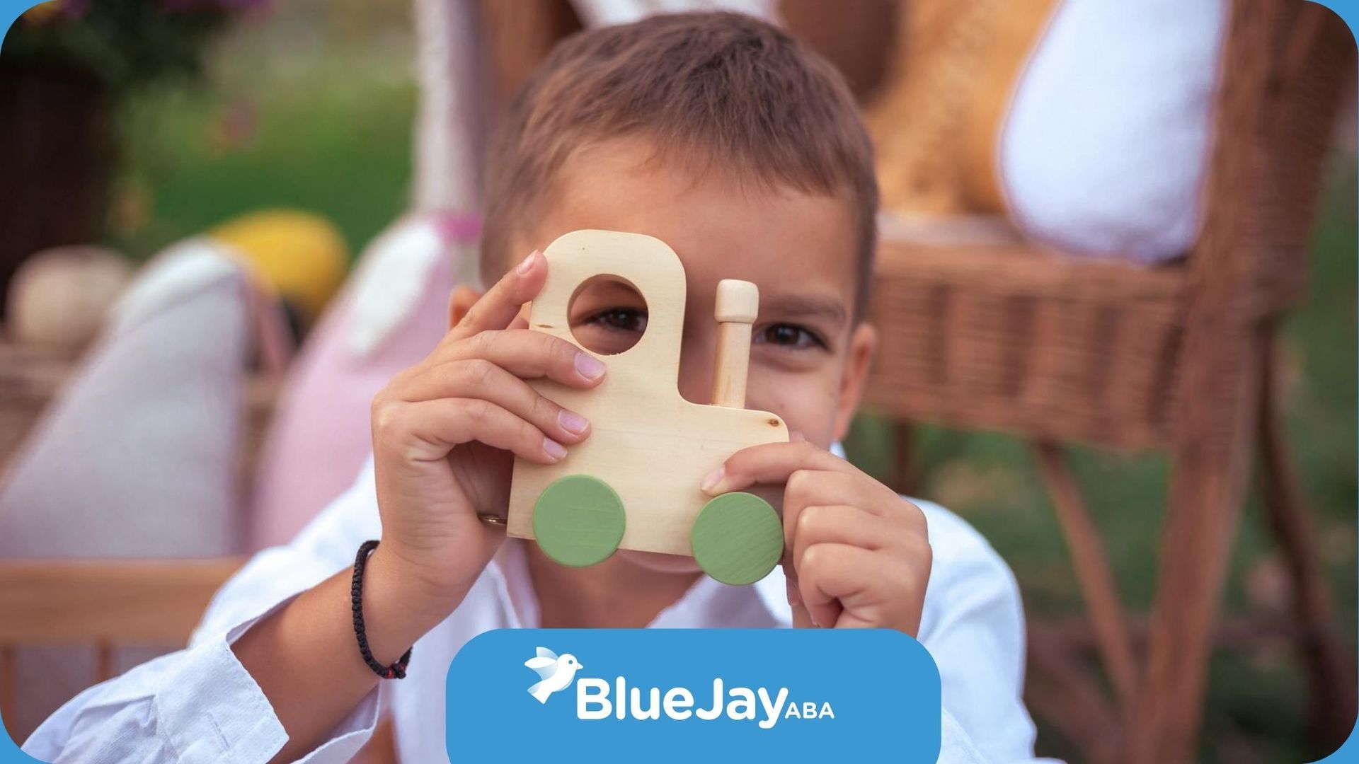 An autistic boy holding a wooden toy train in front of his face while smiling outdoors in NC.