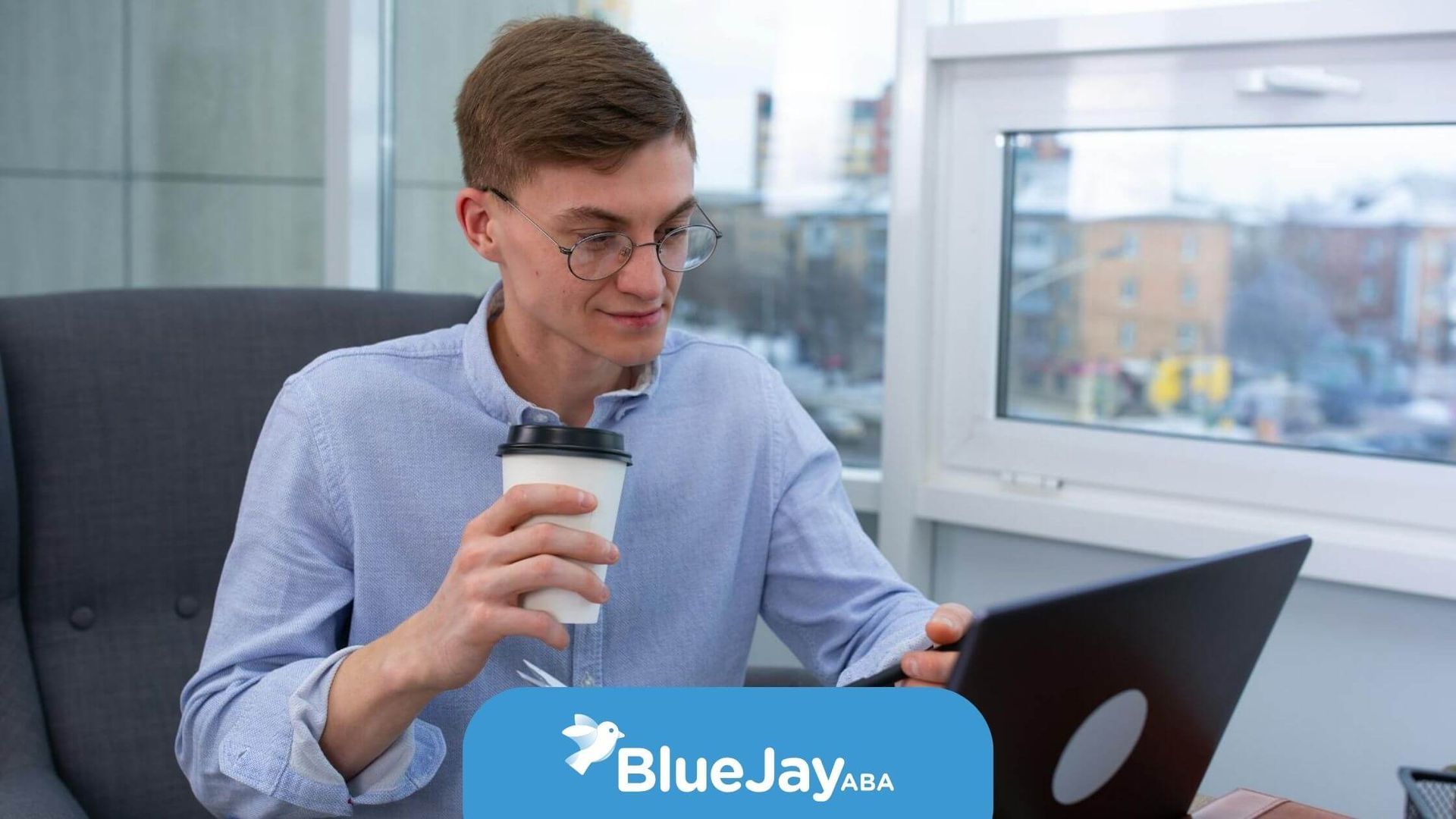Male therapist holding a cup while working on a laptop and planner at a desk in North Carolina.