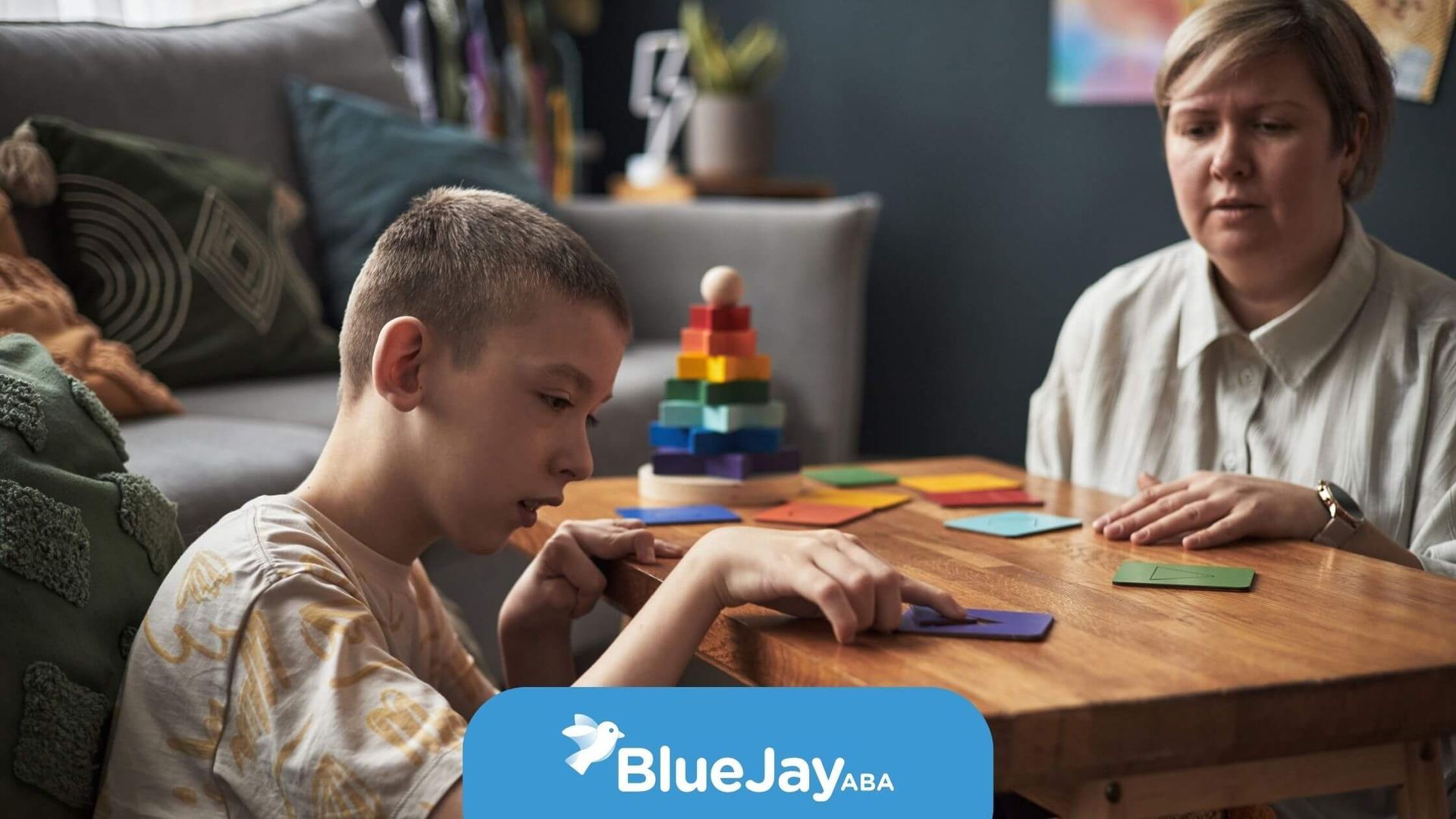 An autistic child and an ABA therapist arranging colorful puzzle cards at a table during therapy.