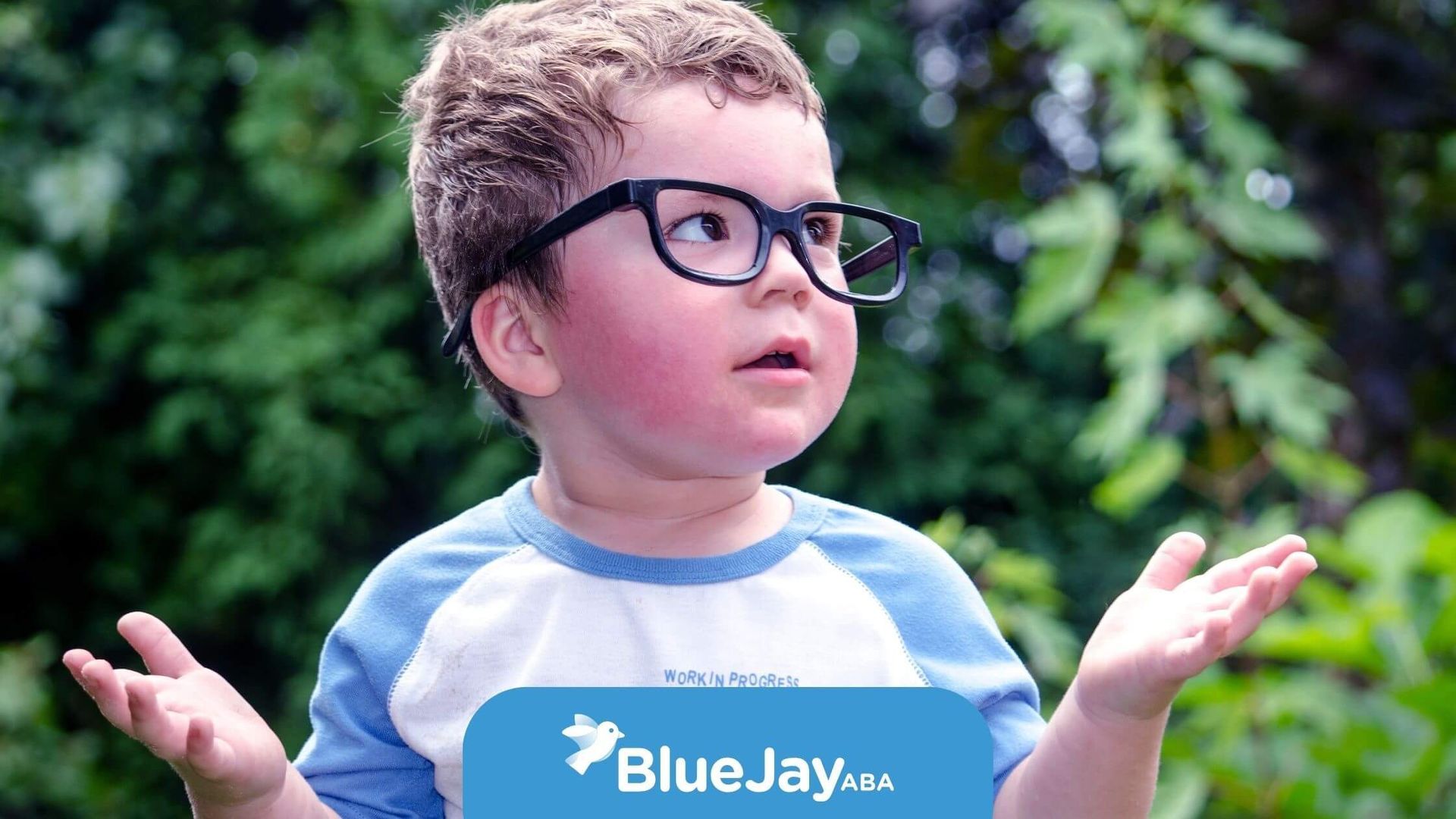 Young autistic child outdoors, looking confused and unsure while making a gesture of uncertainty.