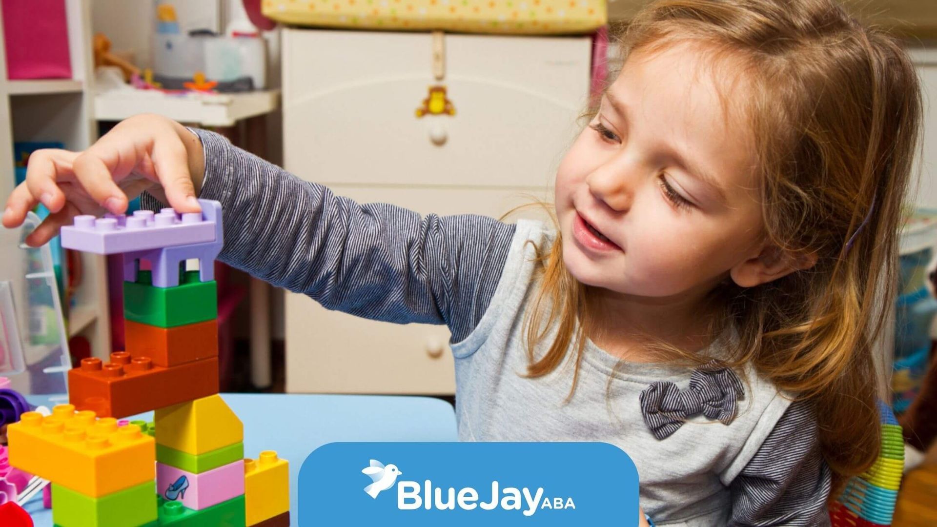 Girl building a tower with colorful toy blocks on a table. She is focused, smiling.