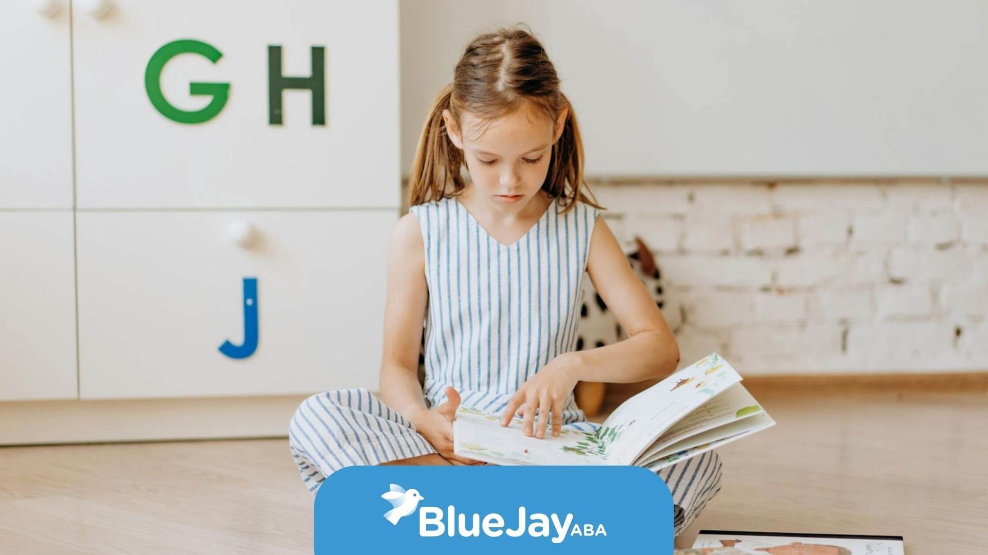Autistic young girl sitting on the floor reading a picture book in a bright room after ABA therapy.