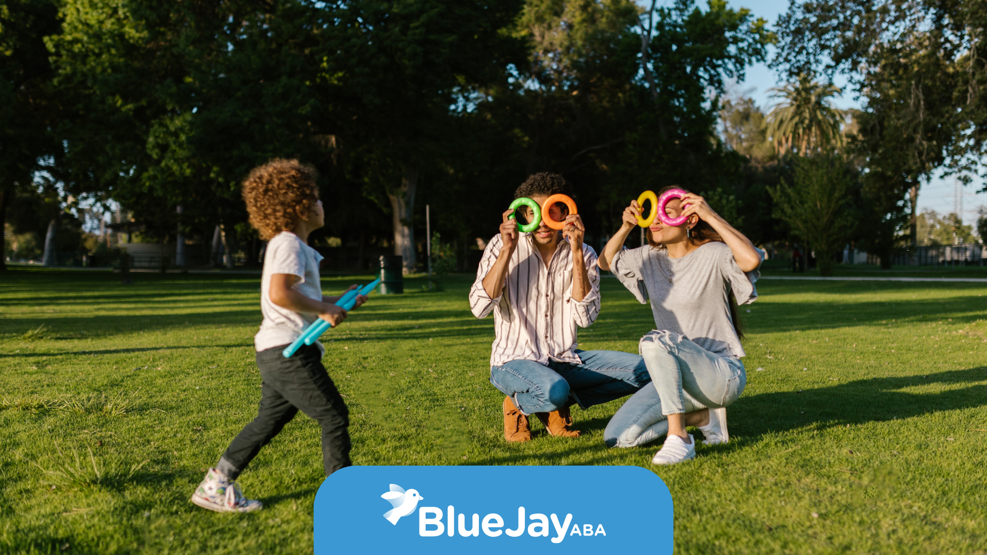 Family playing outdoors with colorful circles, smiling, sunny park.