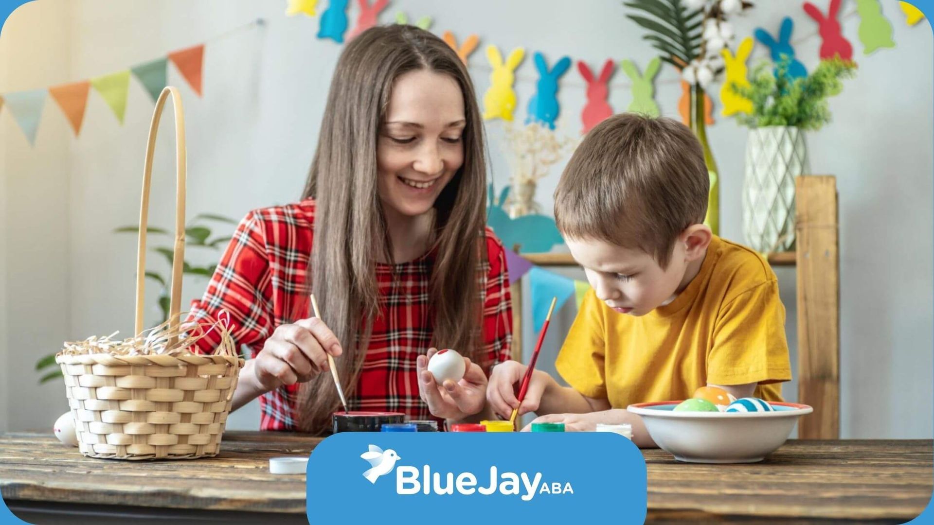 A BCBA and an autistic boy are painting easter eggs at a table in ABA therapy.