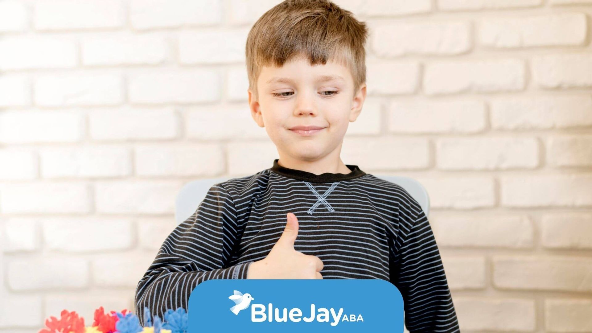 Autistic child giving thumbs up while building with colorful blocks on a table after ABA therapy.
