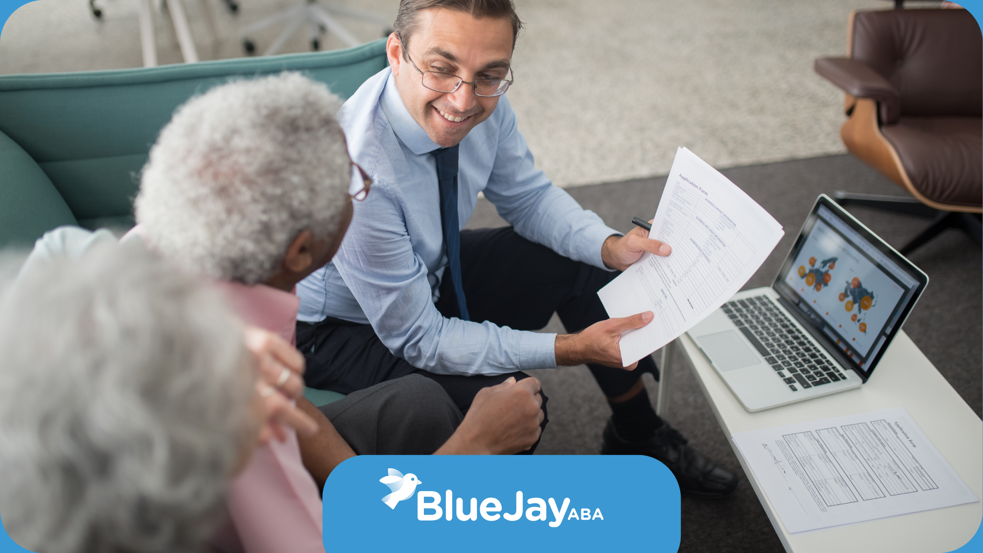 Financial advisor showing documents and laptop to elderly couple in a living room setting.