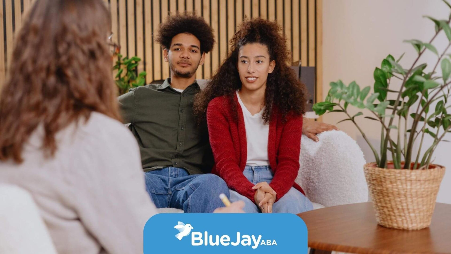 A young couple sits on a couch talking to an ABA therapist during ABA parent training.
