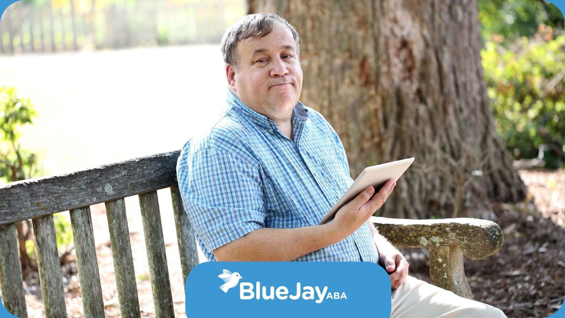 A man is sitting on a bench holding a tablet.