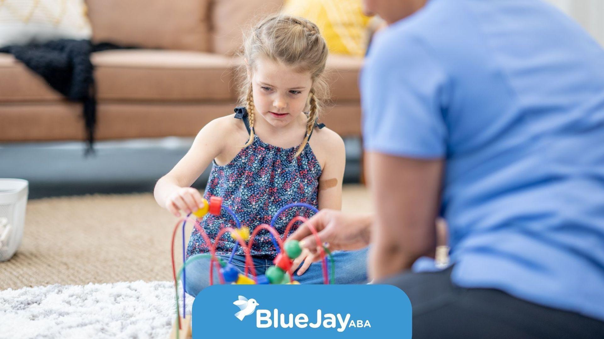 Girl playing with colorful bead maze, adult in blue shirt watches. Indoors on rug.