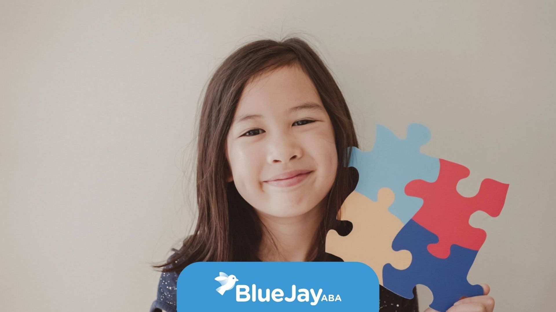 Smiling young girl holding a colorful puzzle piece during ABA therapy.