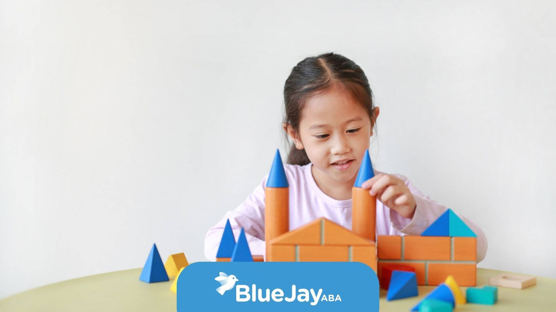 Girl playing with colorful wooden blocks on a table, building a castle.