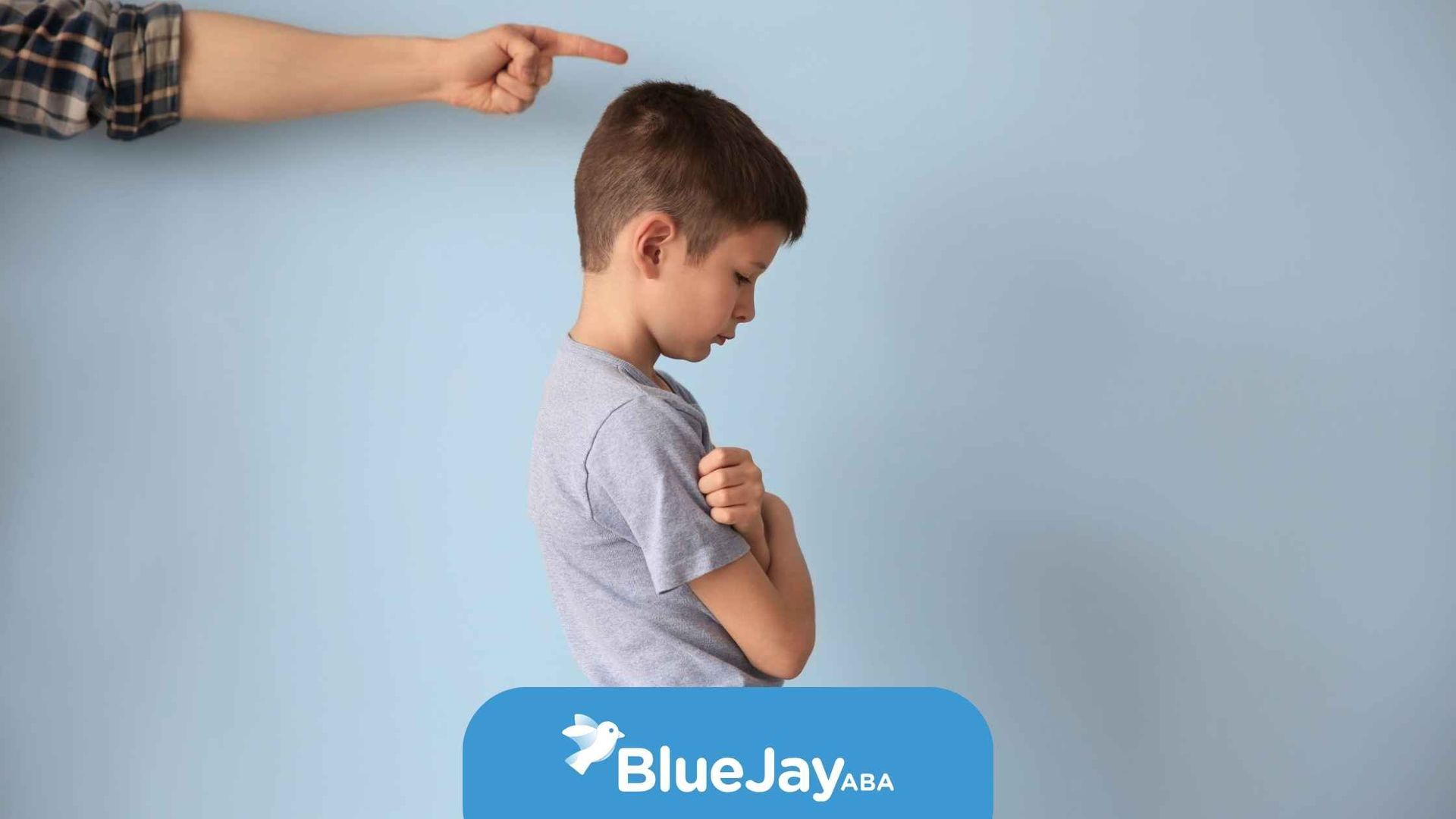 Child being scolded; hand points down. Boy looks downcast with arms crossed. 