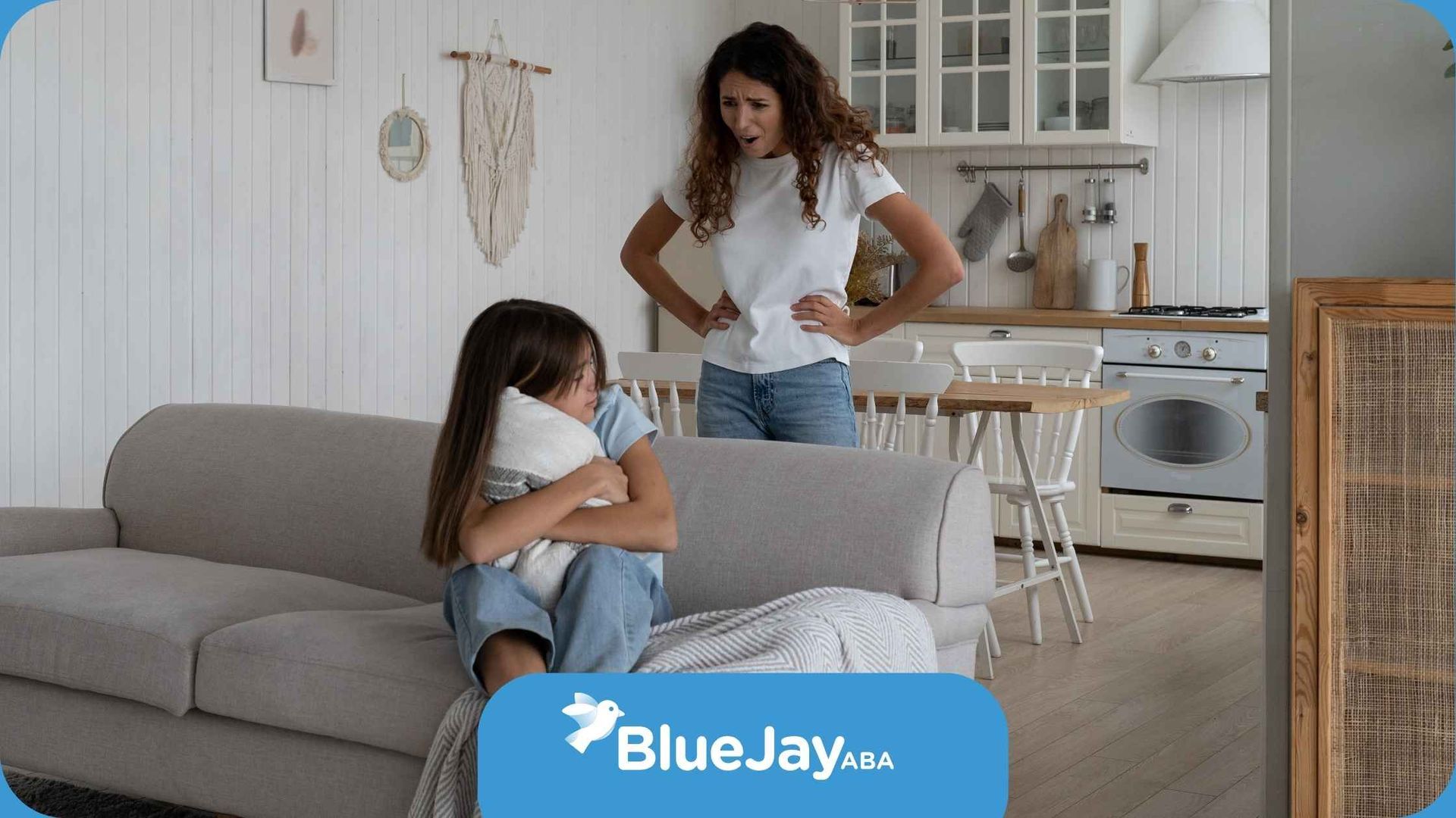 A woman is standing next to a girl sitting on a couch.