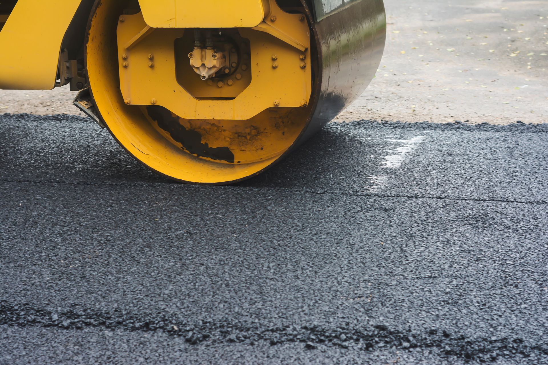 a yellow roller is rolling asphalt on a road .