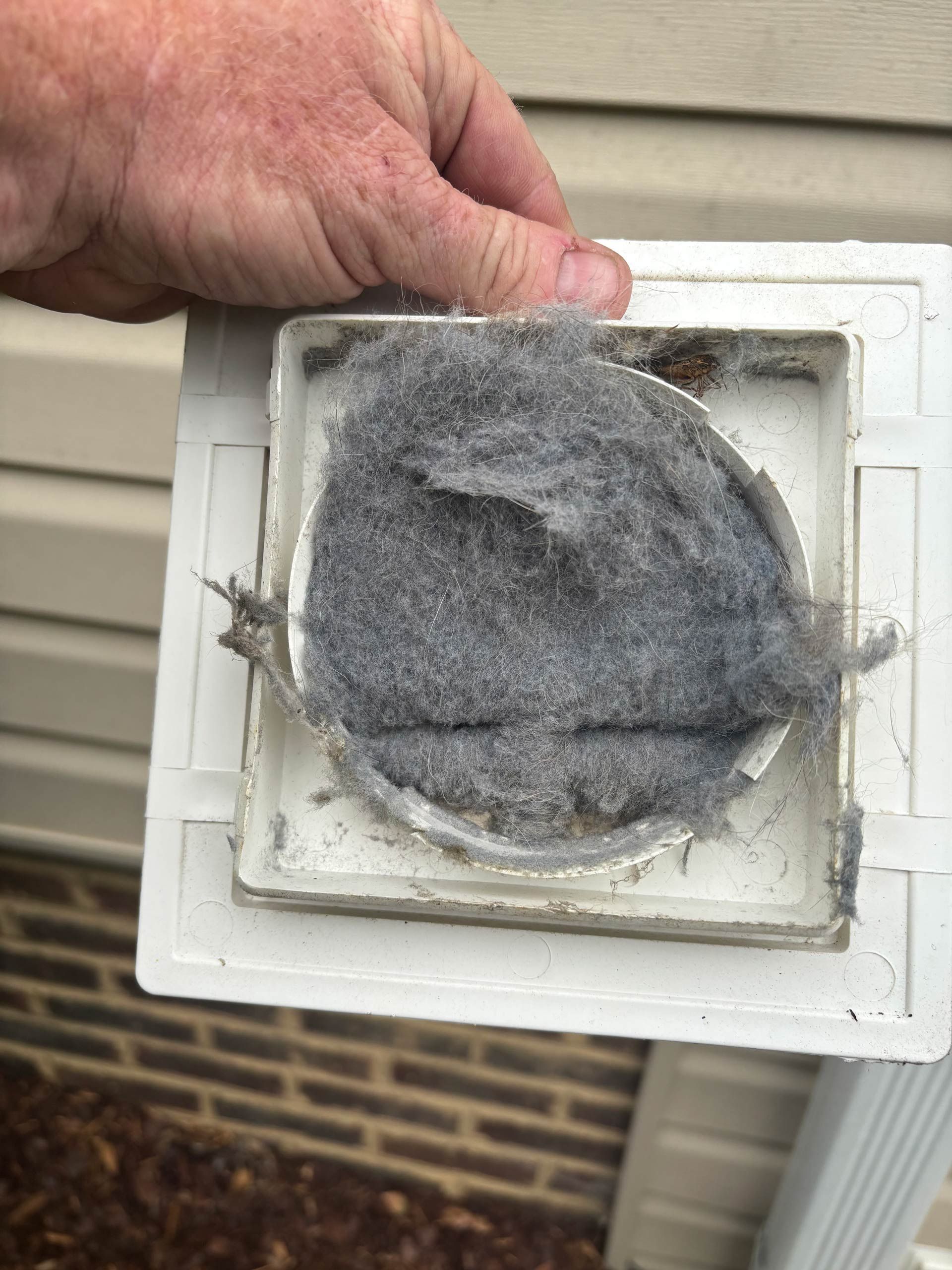 A person is holding a dirty air vent outside of a house.