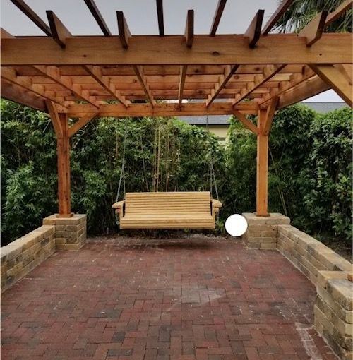 A wooden swing is under a wooden pergola