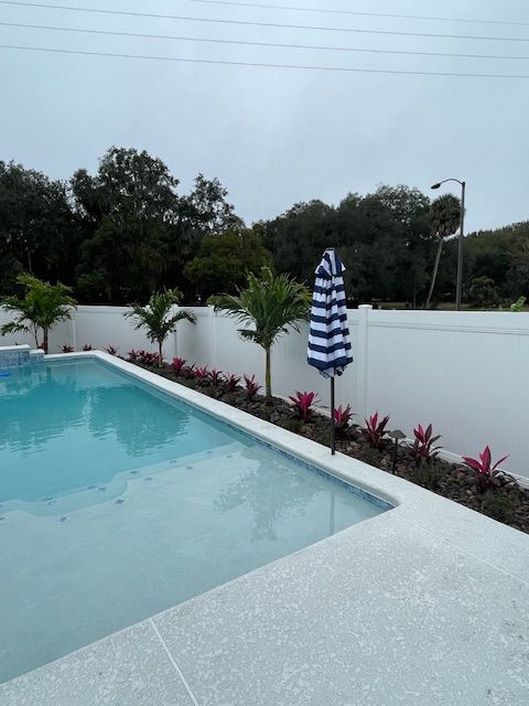 A swimming pool with a white fence and a blue and white striped umbrella