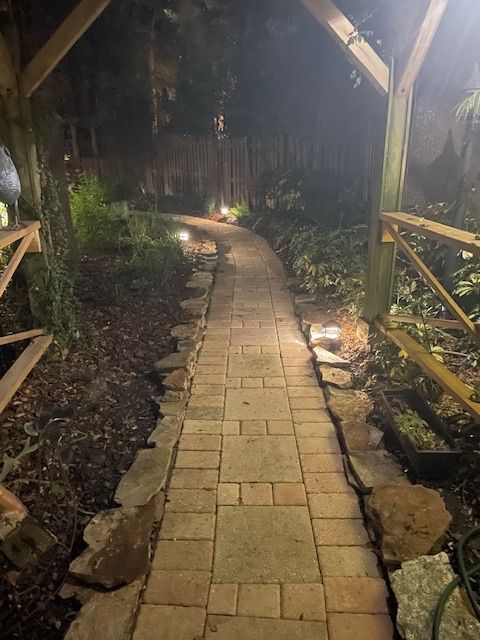 A brick walkway is lit up at night in a garden.