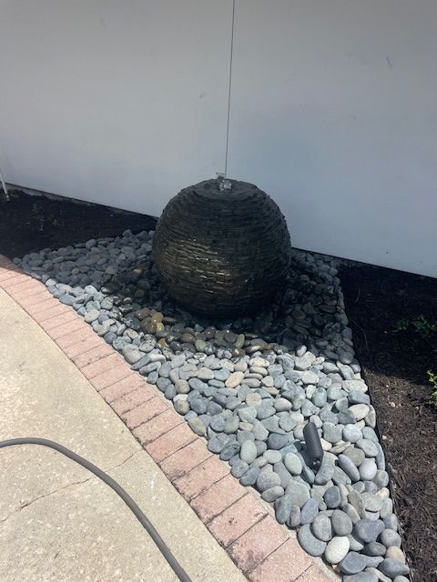A fountain is sitting on a pile of rocks next to a brick walkway.