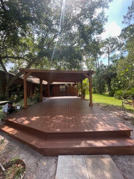 A wooden deck with stairs and a pergola in front of a house.