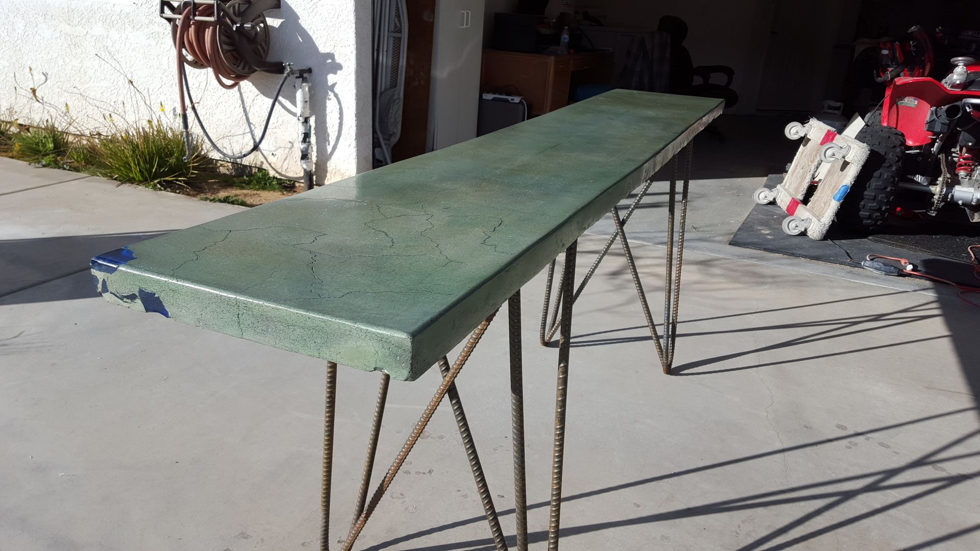 A green table is sitting on a concrete driveway in front of a garage.