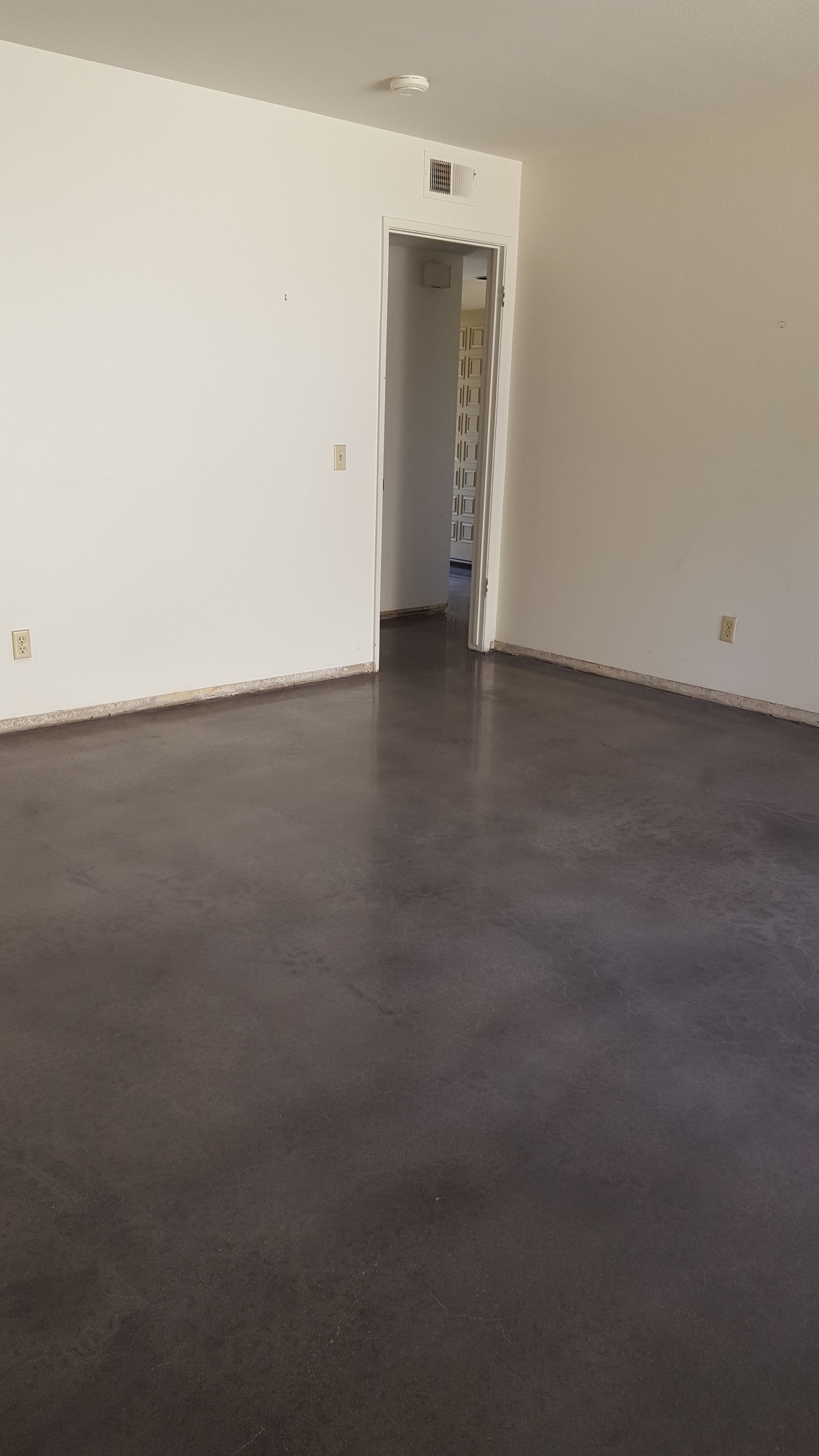 An empty living room with a black floor and white walls.