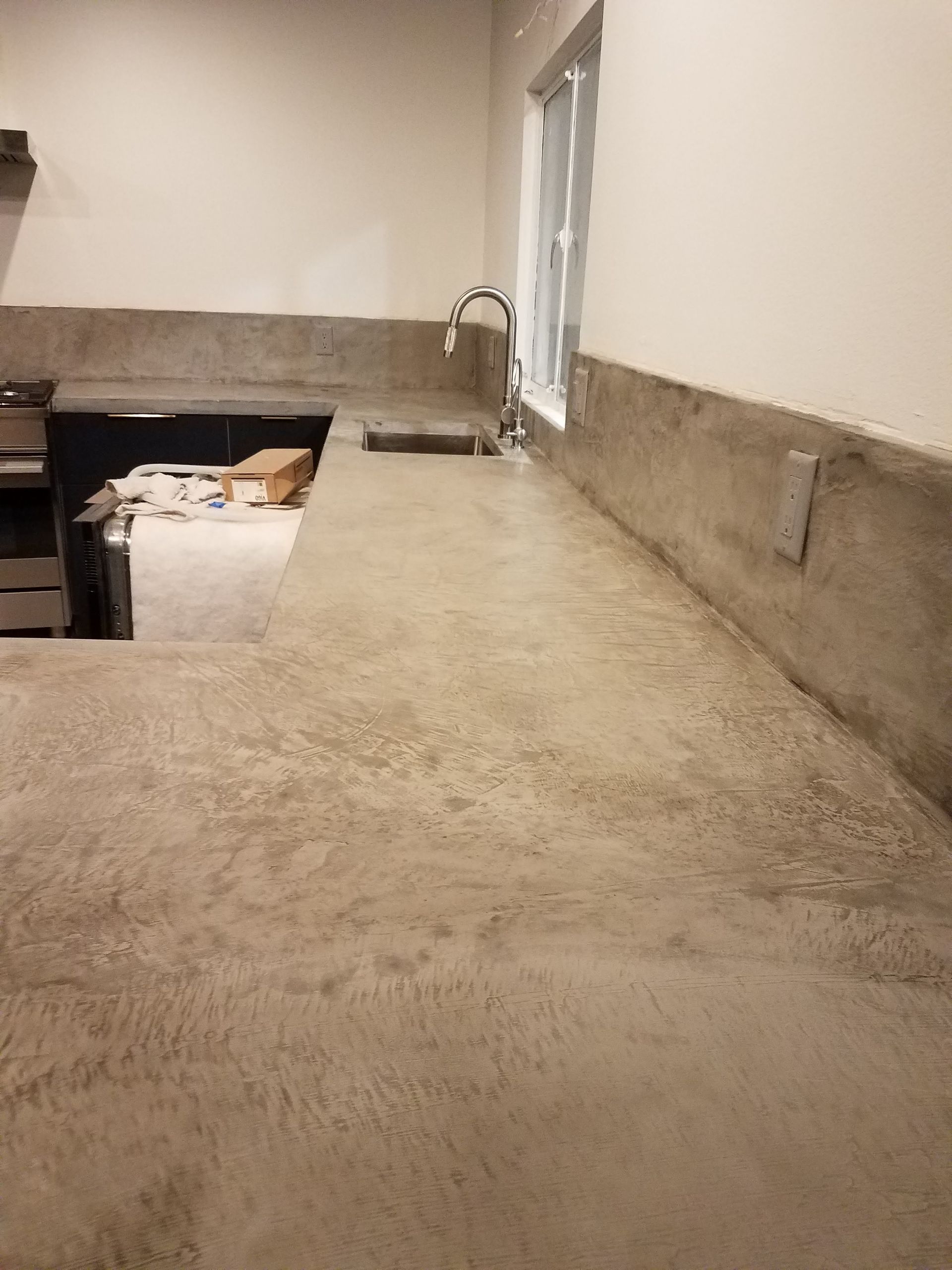 A kitchen with a concrete counter top and a sink.
