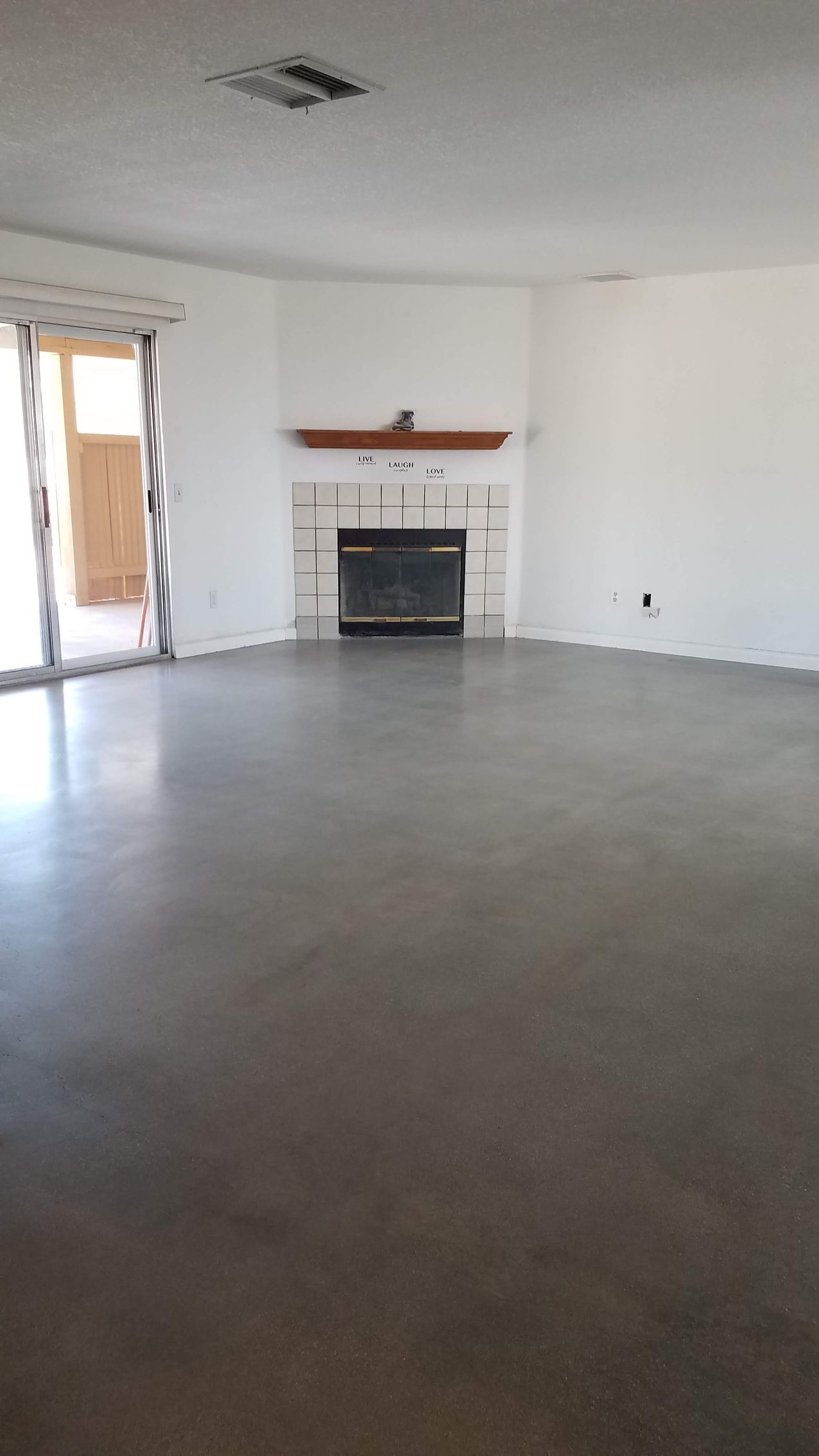 An empty living room with a fireplace and sliding glass doors.