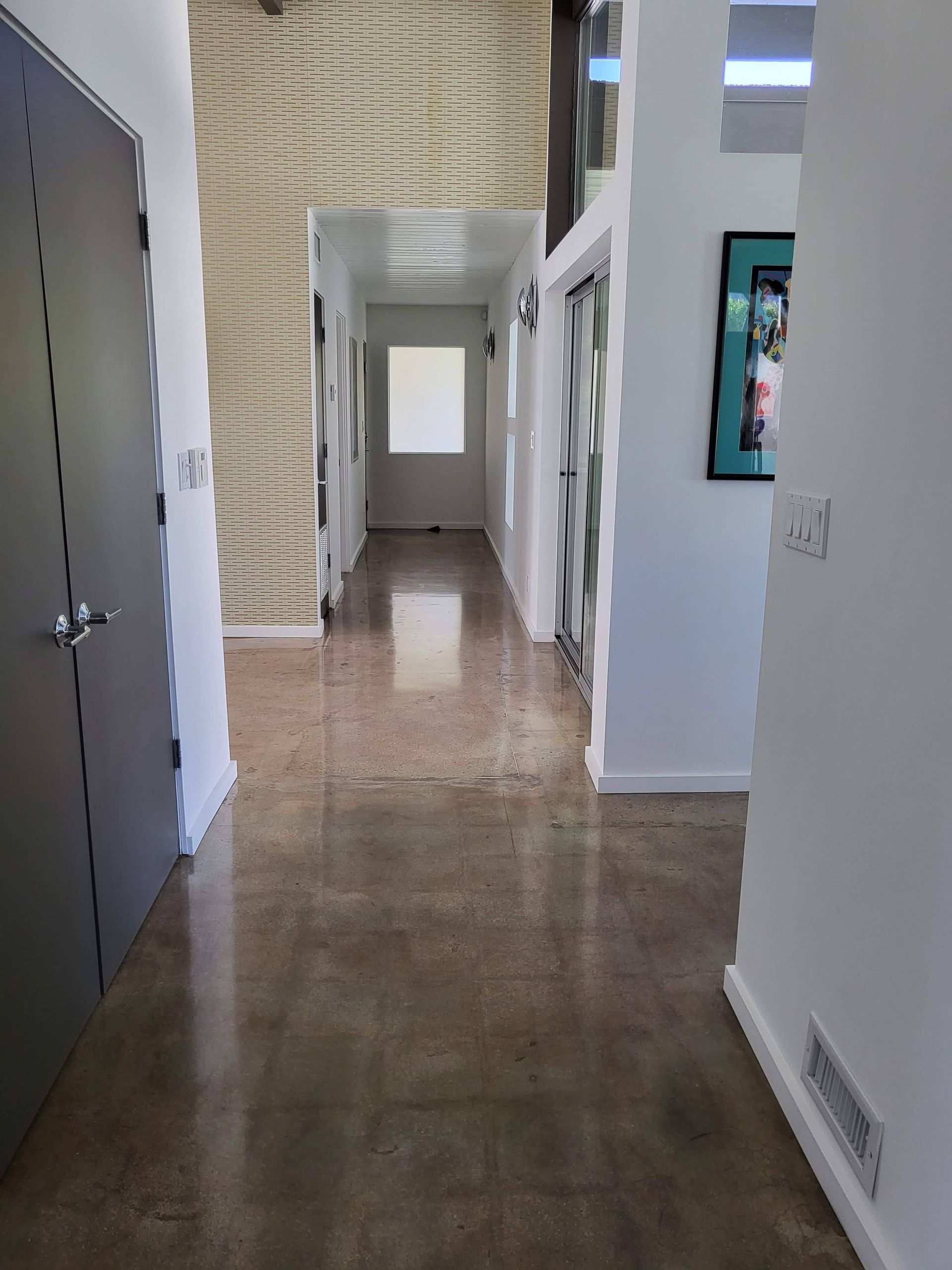 A long hallway in a house with a staircase and a painting on the wall.