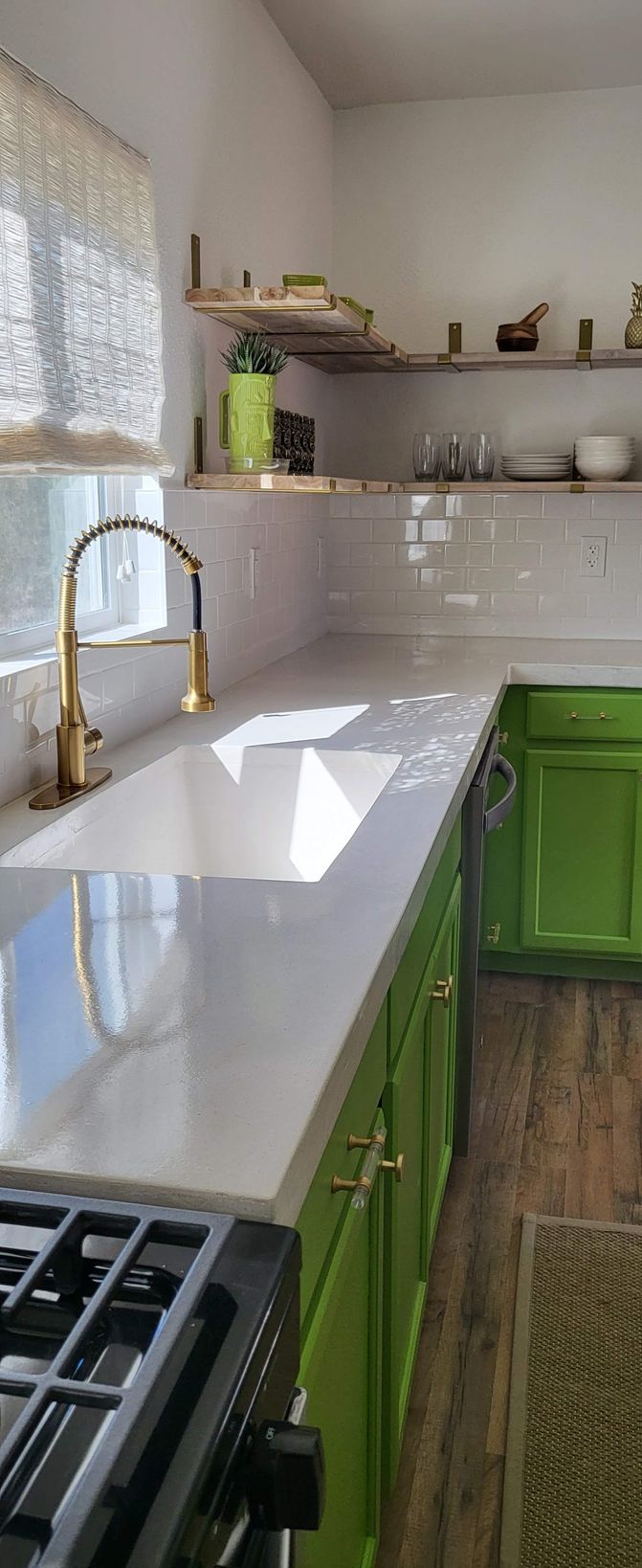 A kitchen with green cabinets , a stove , a sink , and a window.