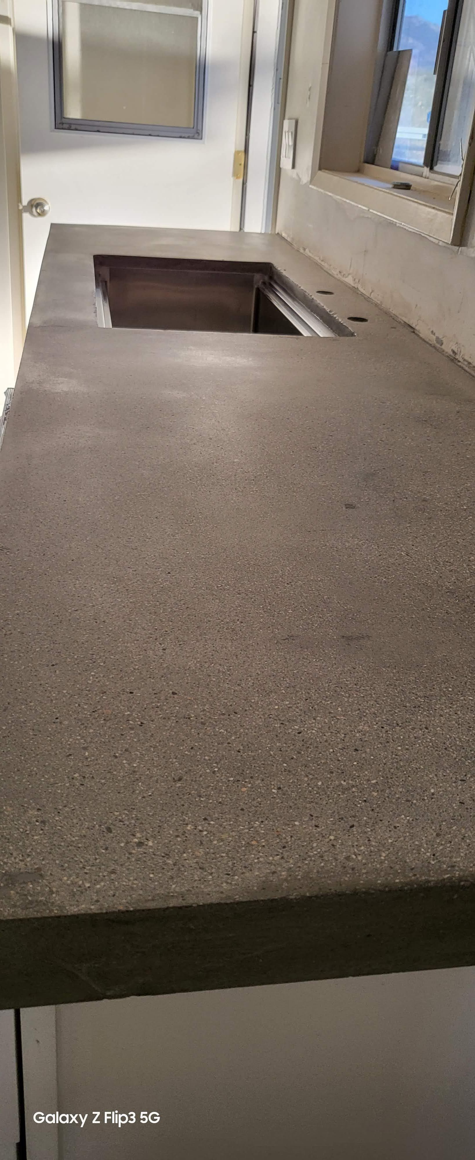 A kitchen counter with a sink and a window in the background.