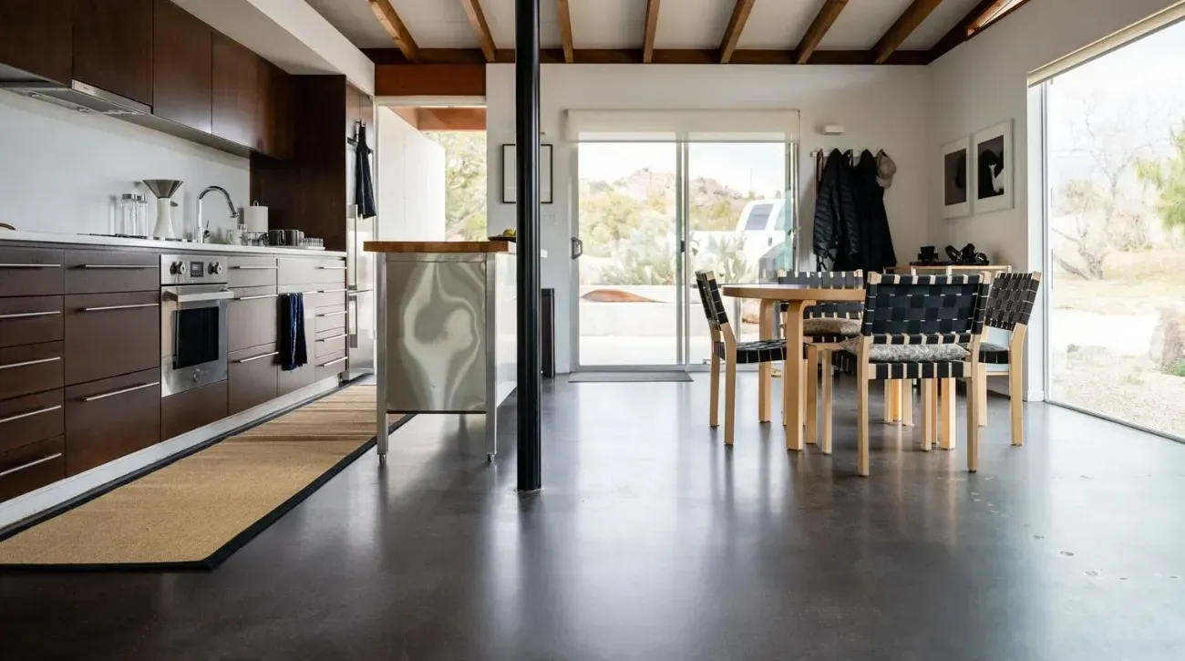 A room with a concrete polished floor , a table , and a door.