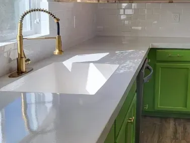 a kitchen sink on a concrete countertop with a gold faucet and green cabinets in Yucca Valley, South California.