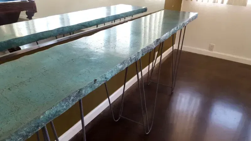 Long, turquoise-colored concrete table with hairpin legs, in front of a wall.