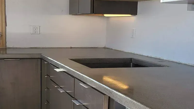 Gray concrete countertop in a modern kitchen with gray cabinets and white walls.