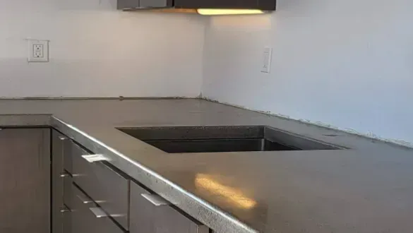 A kitchen countertop with a rectangular cutout for a sink, featuring smooth grey surfaces and dark cabinets.