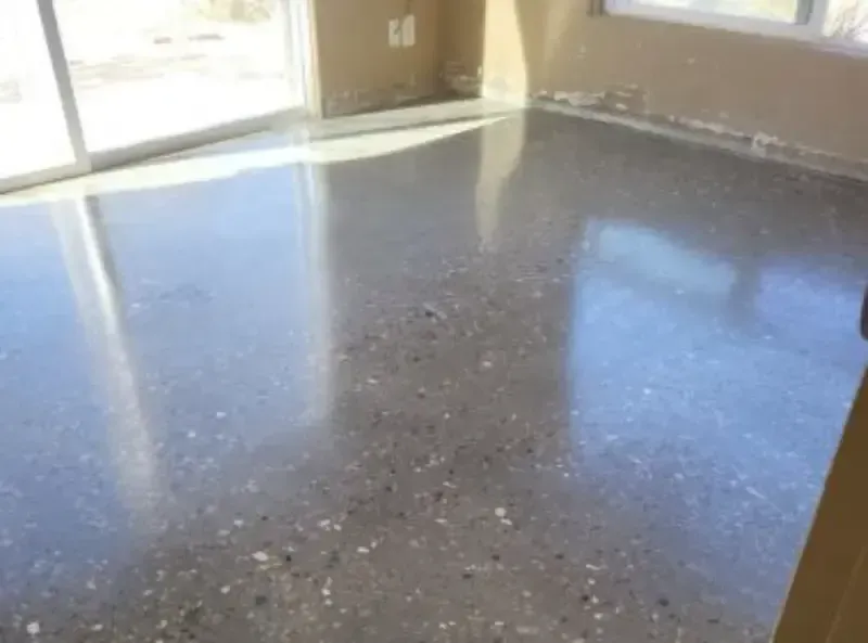 Polished, speckled concrete floor in a room with light-colored walls and large glass doors.