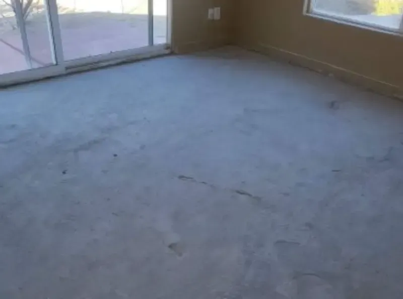 Unfinished concrete floor in a room with a sliding glass door and windows.
