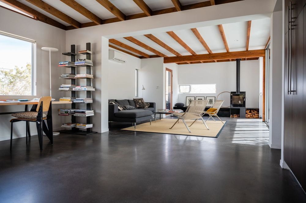 A living room with a couch, chairs, a desk, a fireplace, and a polished concrete floor.