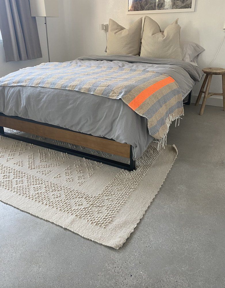 A bedroom with a bed and a rug on the polished concrete floor.