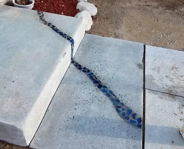 Concrete steps with blue glass inlay, adjacent to a red brick wall and landscaped area with mulch.